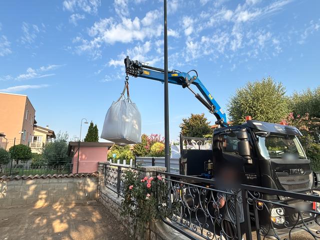 Camion con gru che scarica un big bag di materiale vicino al giardino