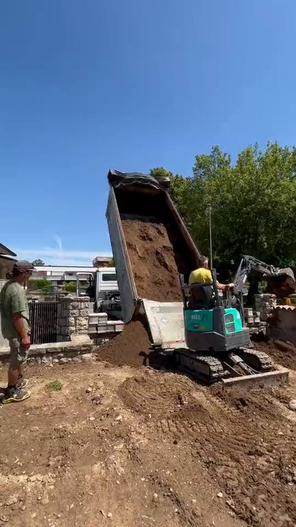 Camion che scarica la terra e miniescavatore che la stende